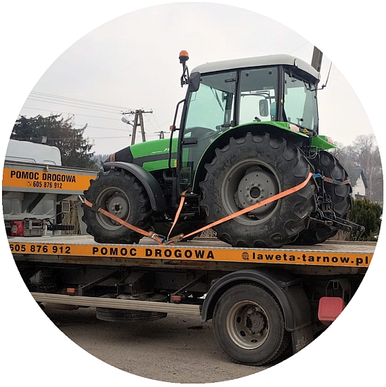 Zielony traktor na platformie lawety przypięty pasami transportowymi. Transport ciągnika na terenie Tarnowa. 